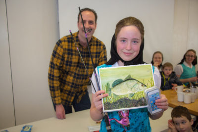 Student holding artwork displaying a drawing of a fish